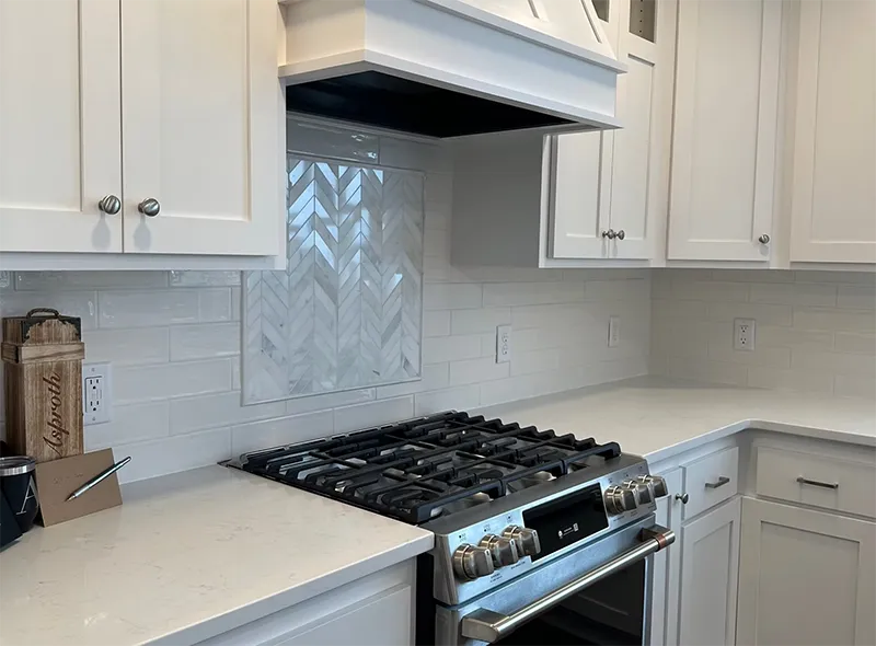 A bright, modern new construction kitchen featuring white cabinets, a white subway tile backsplash, and a stainless steel gas range with a matching hood.